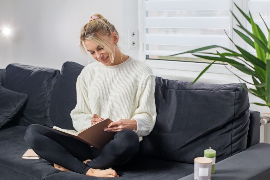 Smiling woman journaling on couch in cozy home